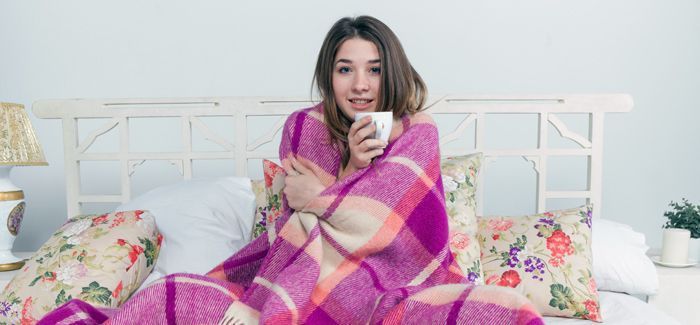 Sick woman covered with blanket holding cup of tea